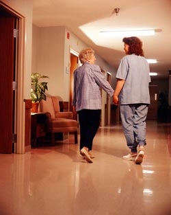 A caregiver walking a woman down a hallway.